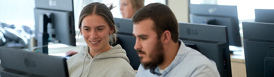 Two young adults discuss something shown on a laptop.