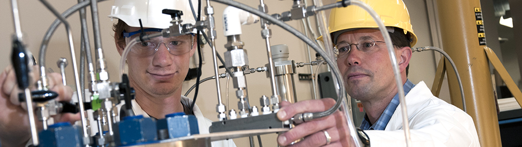 Two engineers in hard hats monitor distilling equipment.