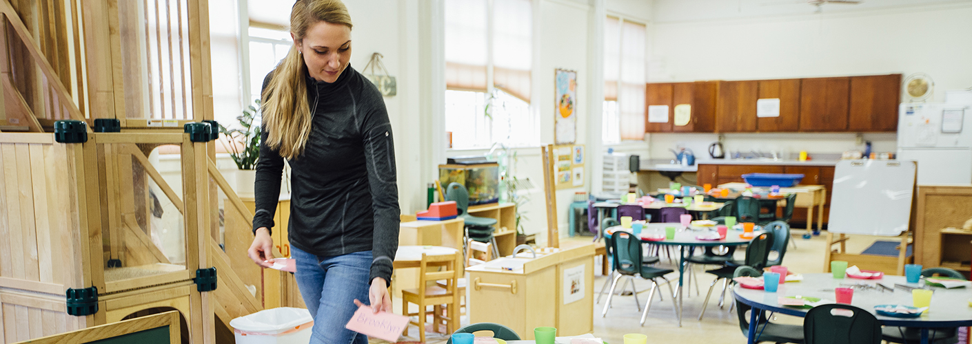 A woman walks around a classroom, preparing for students.