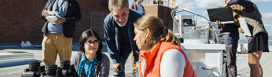 A group of students consult with a professor on top of a roof.