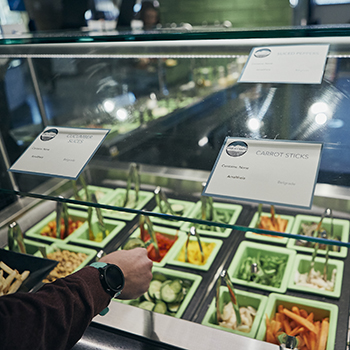 person using tongs to plate food out of the salad bar area